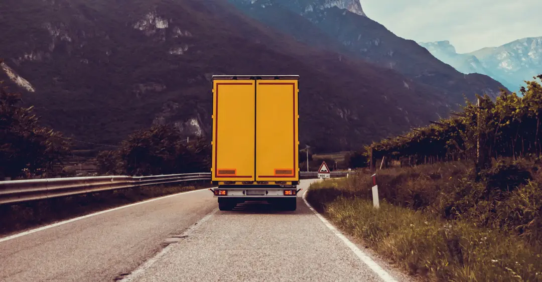 Camión de carga avanzando por una carretera de montaña rumbo a su entrega