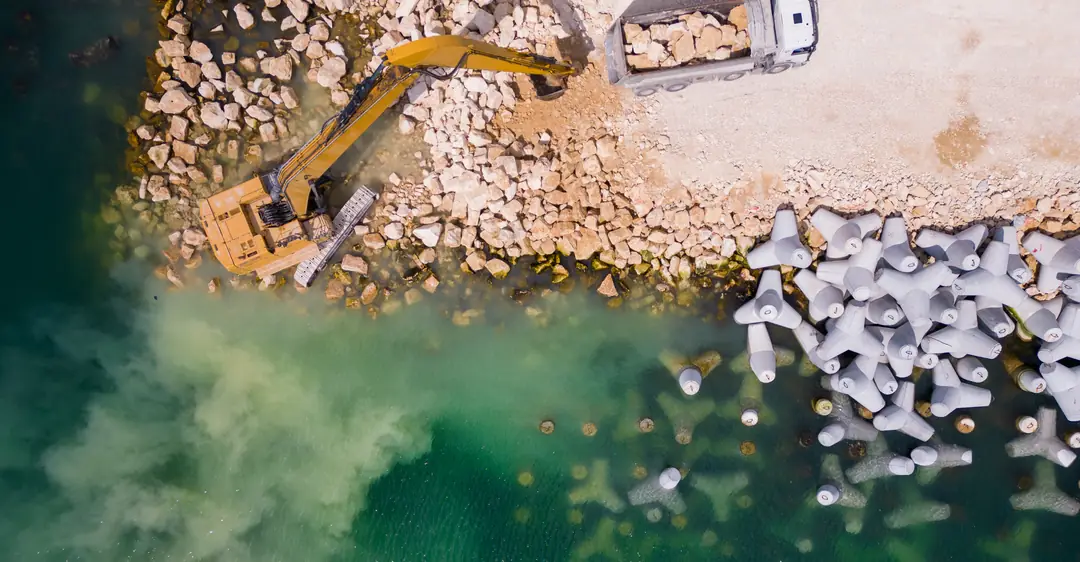 Vista aérea de una excavadora y un camión de volteo construyendo una escollera junto al mar