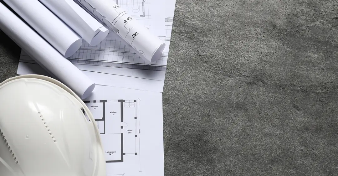 Casco de seguridad y planos ejecutivos extendidos sobre una losa de concreto