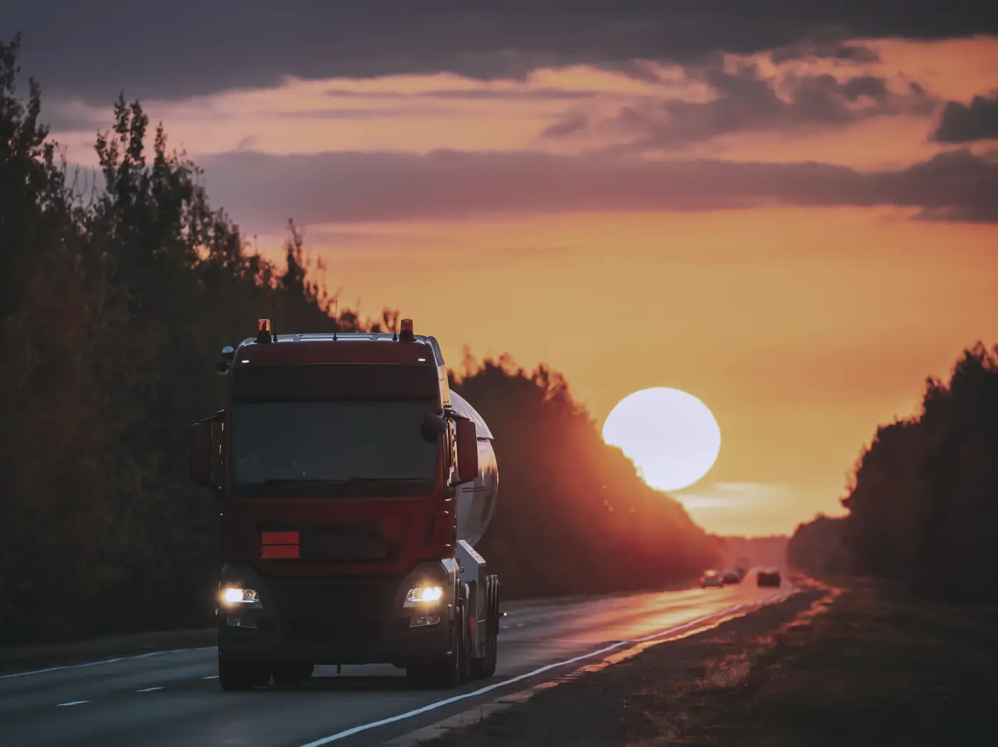 Tractocamión avanzando por una carretera al atardecer, con el sol sobre el horizonte